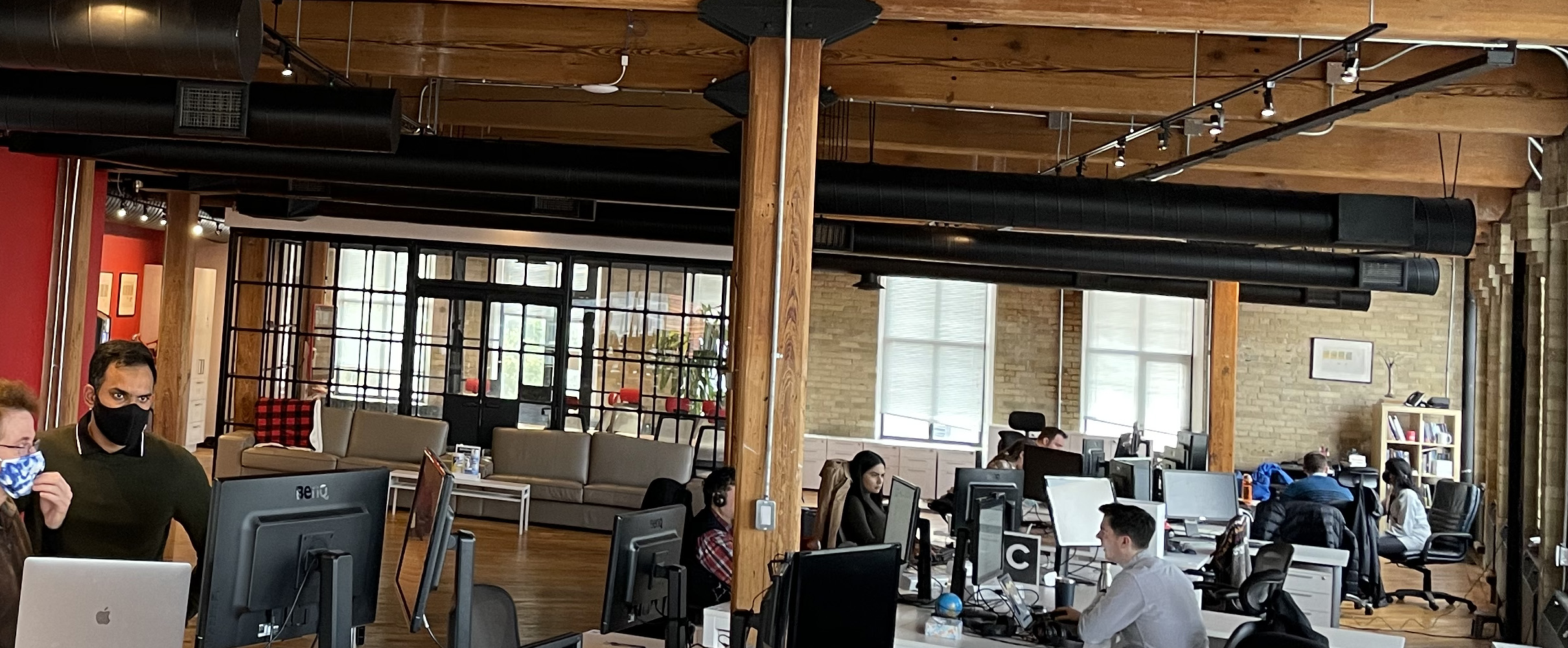 Masked Uncharted staff confer at socially distanced workstations in an open-concept office.